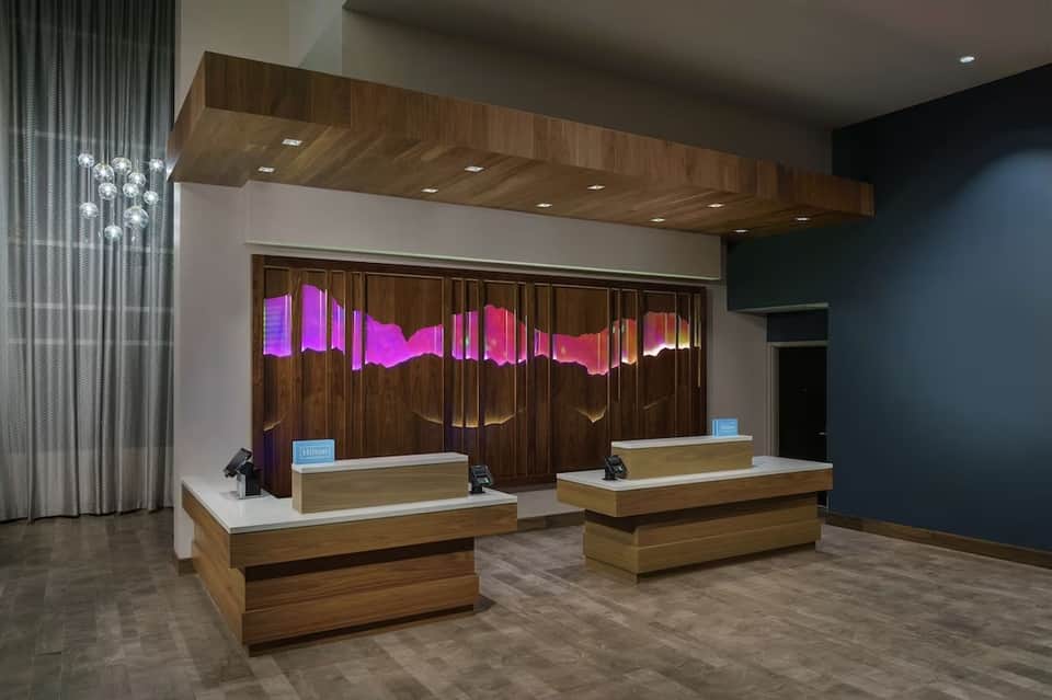 Modern hotel reception desk with dual white counters, wooden soffit, pink neon signage, and ambient lighting