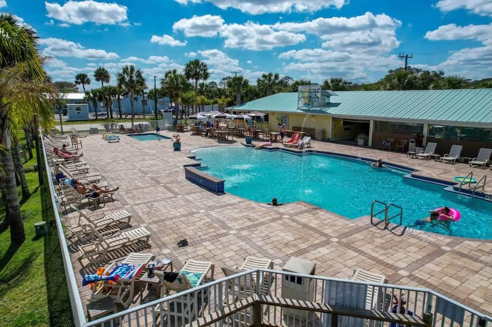 Expansive resort pool with palm trees, covered pavilion, lounge seating, and landscaped grounds