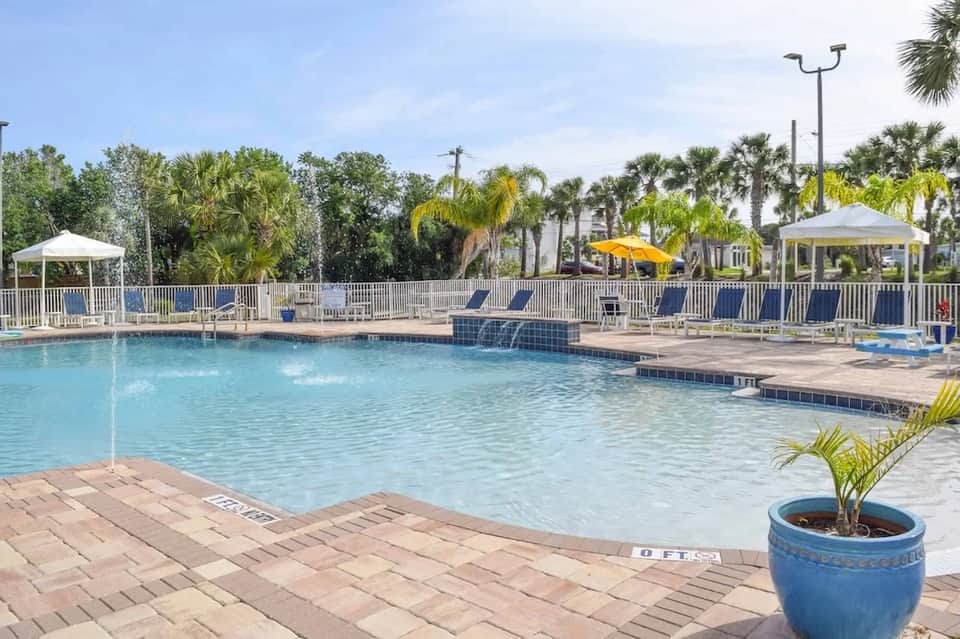 Lakeside resort pool with lounge chairs, umbrellas, white railings, and palm trees
