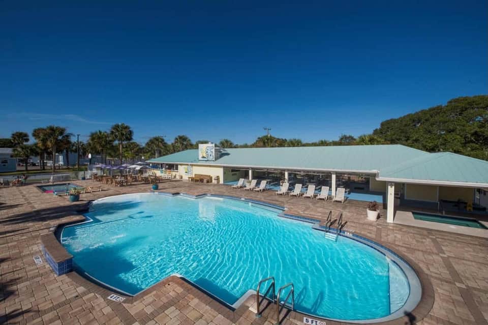 Resort pool complex with pale blue water, covered pavilions, and palm tree surroundings