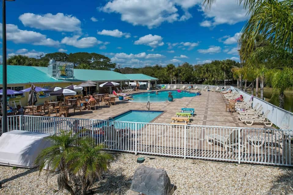Resort pool area with turquoise water, palm trees, lounge chairs, and covered bar seating