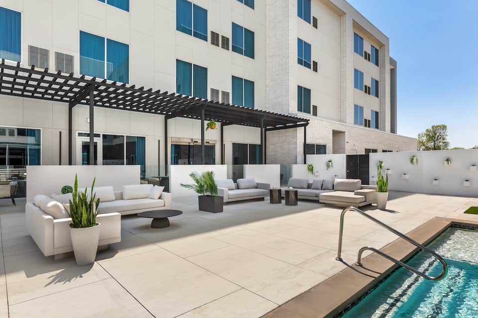 Modern resort terrace with white lounge furniture, pergola, and infinity pool with city view