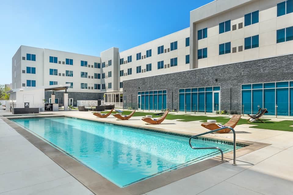 Modern resort building with lap pool, lounge chairs, and contemporary architecture under clear sky