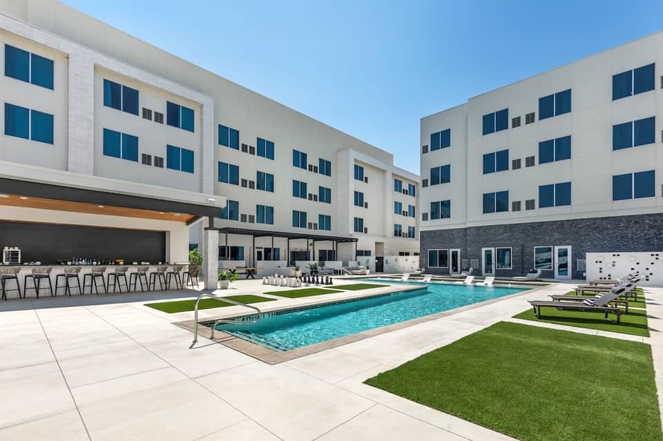 Contemporary hotel courtyard pool with green lawn, loungers, and building facade