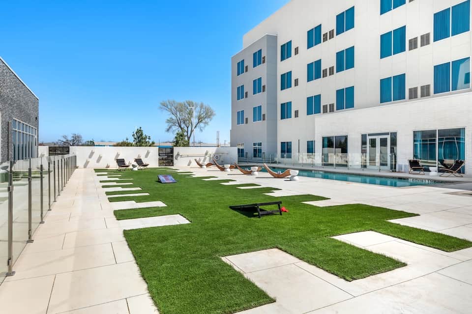Contemporary apartment building rooftop pool with patio lounge, grass sections, and sky view