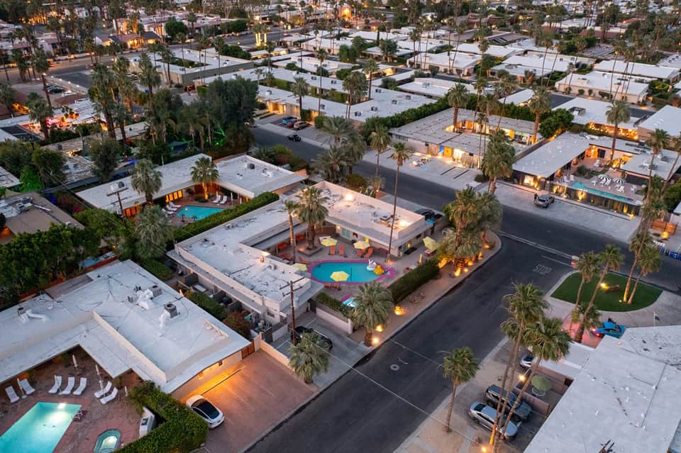 Aerial view of mid-century modern resort community with multiple pools and palm trees at dusk