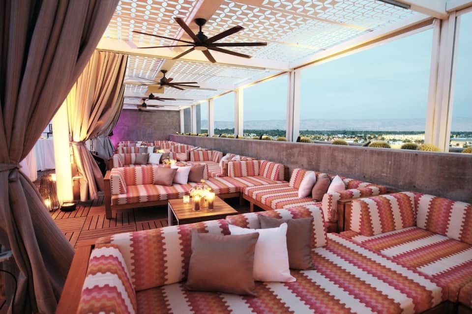 Modern rooftop lounge with pink striped seating, ceiling fans, floor-to-ceiling windows with valley views