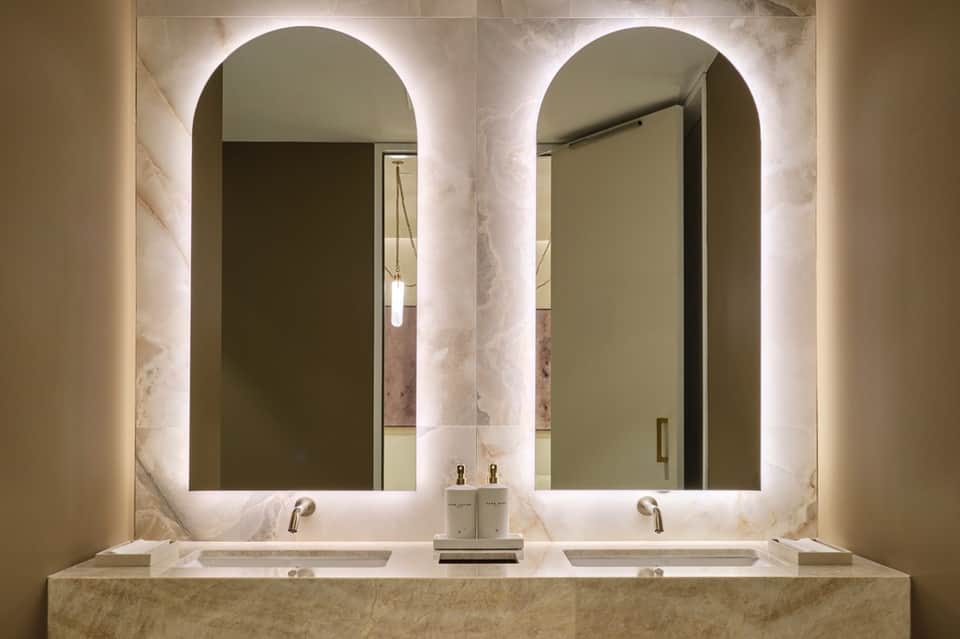 Luxury bathroom with dual vessel sinks, marble countertop, and two arched illuminated mirrors