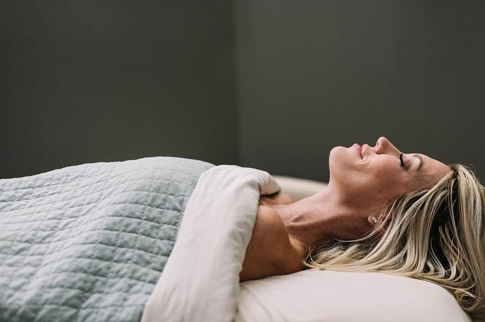 Woman relaxing in bed with soft white pillows and light green quilted bedding