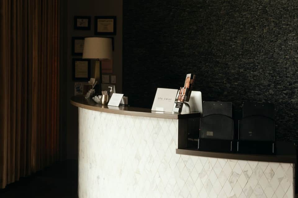 Modern spa reception desk with white marble counter and black textured wall backdrop