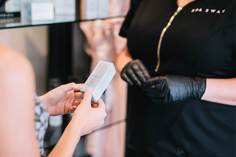 Close-up of woman's hands receiving spa product in white box from spa staff member wearing black uniform