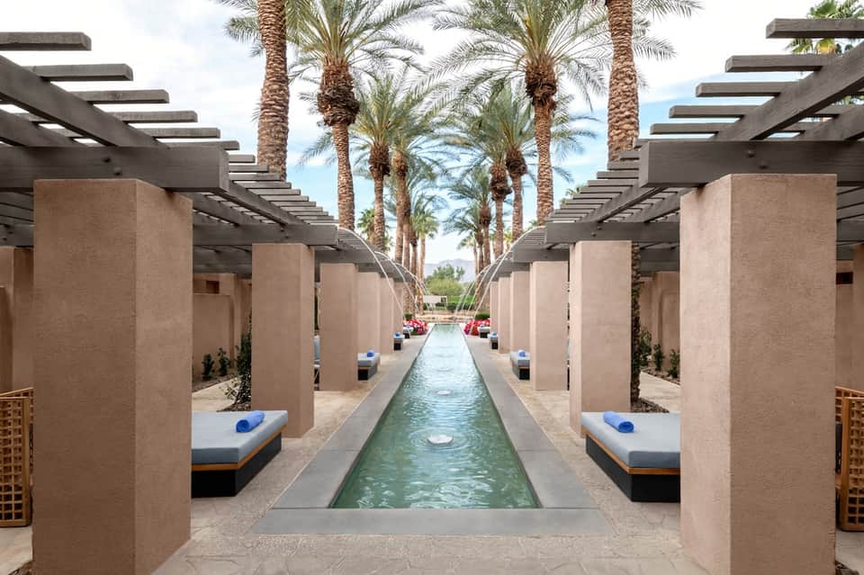 Luxurious spa corridor with slotted pergolas, palm trees, and narrow reflecting pool with lounge beds
