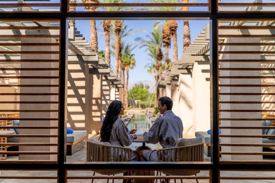 Two guests relaxing in lounge chairs under modern pergola with palm tree views