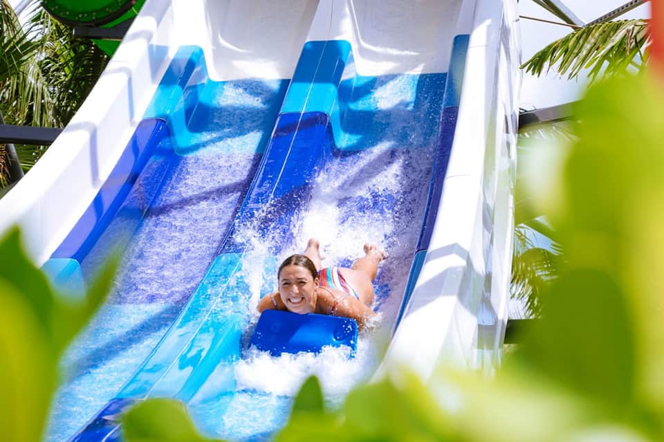 Child sliding down a blue water slide at a tropical resort with palm trees