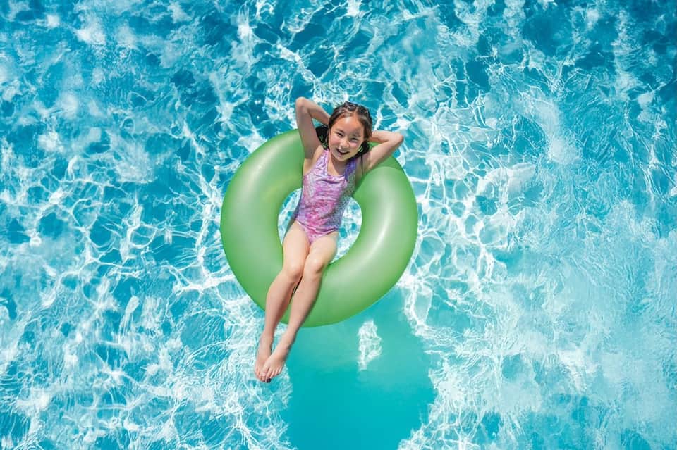 Overhead view of young girl floating on green inflatable ring in bright turquoise swimming pool