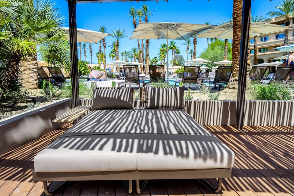 Cabana bed with striped shade canopy overlooking desert pool and palm trees