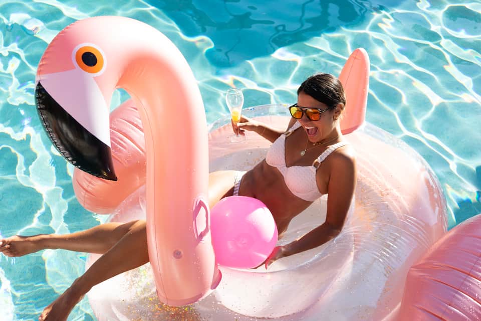 Woman enjoying flamingo float in bright blue pool with champagne glass