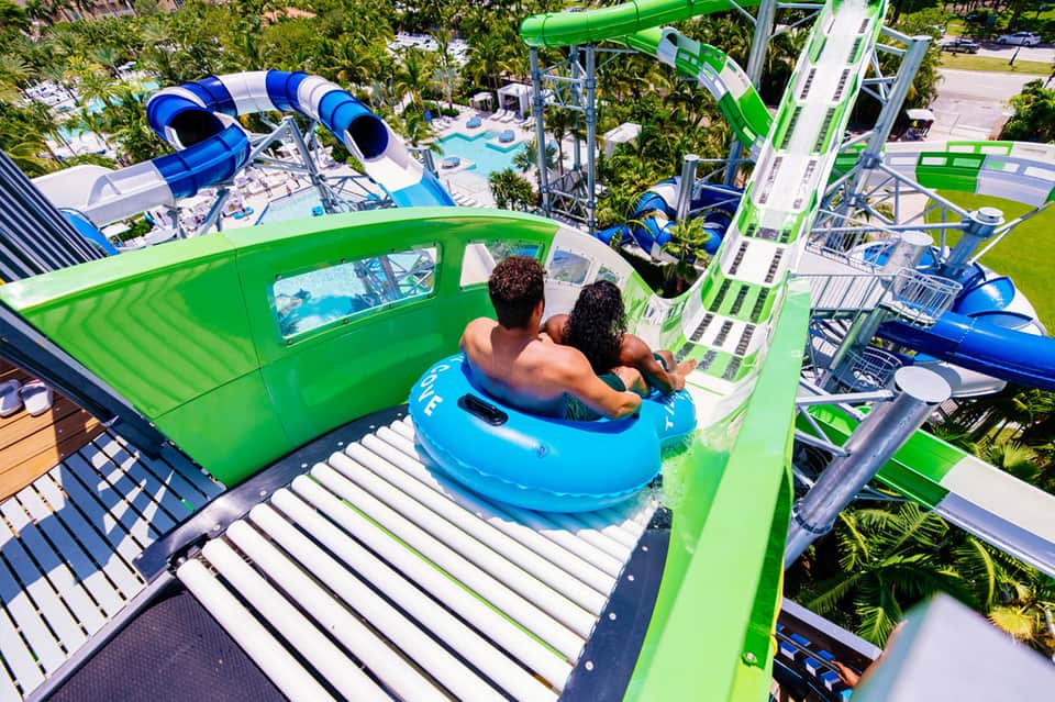 Couple on blue tube descending green water slide at tropical water park
