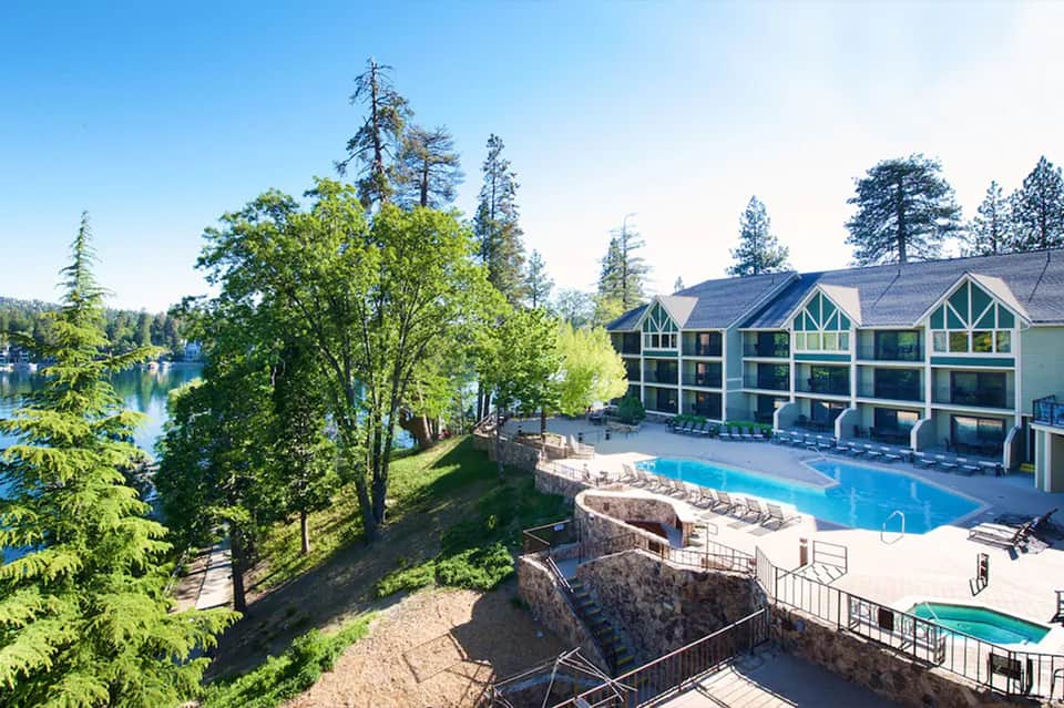 Resort exterior with lake views, alpine architecture, blue pool, lounge chairs, and surrounding forest