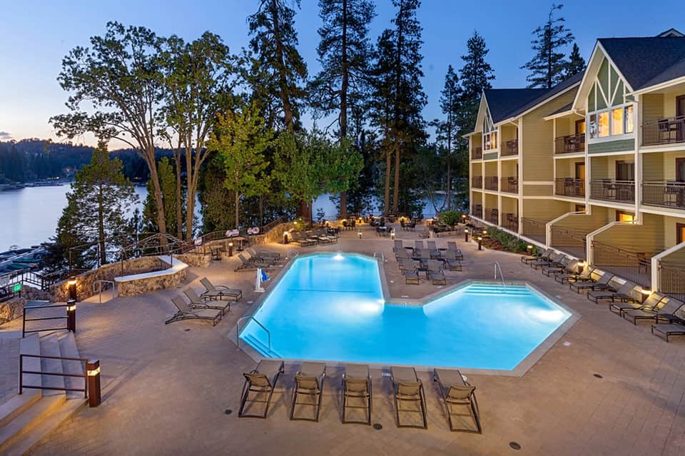 Resort pools at dusk with fire pit, lounge chairs, and lake view with illuminated hotel building