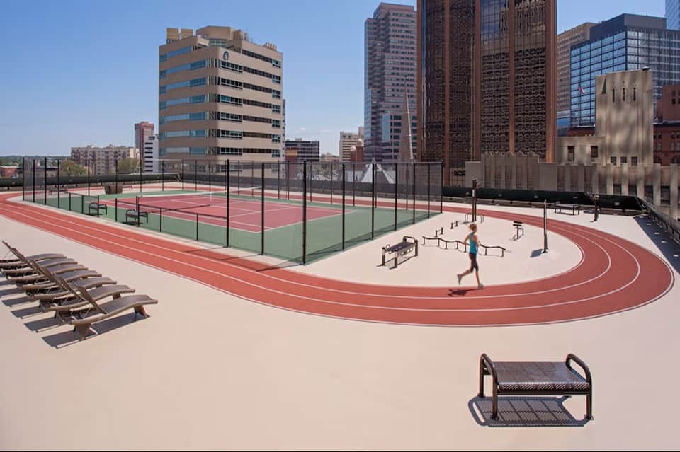 Urban rooftop with running track, tennis courts, exercise area, and city skyline views