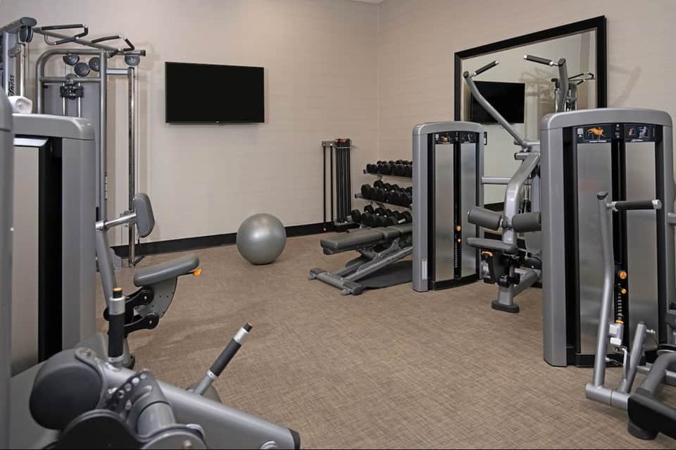 Modern fitness center with cardio equipment, weights, and flat-screen TV