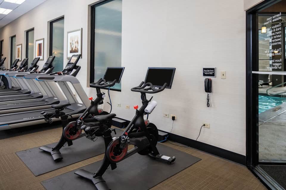 Fitness center with spinning bikes, treadmills, and large windows overlooking pool area