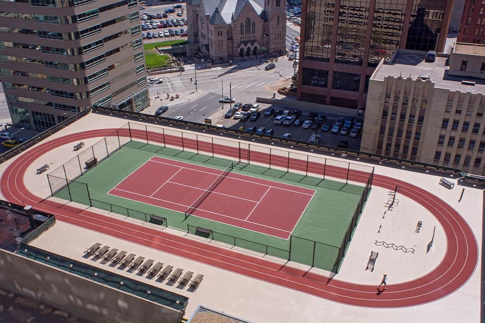 Rooftop running track and tennis courts with city skyline, church, and downtown buildings visible