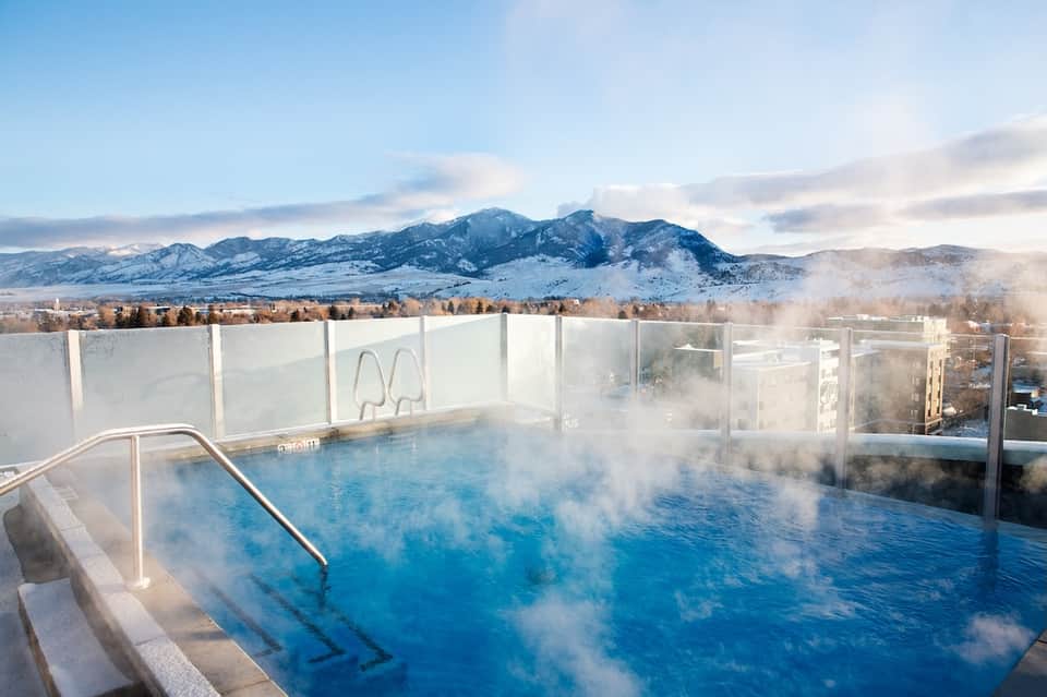 Steaming outdoor hot spring pool on rooftop with snow-capped mountains in background