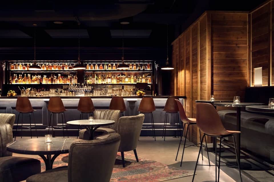 Upscale hotel bar with illuminated shelving, brown leather seating, and dark wood accents