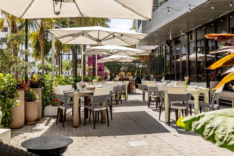 Outdoor dining area with cream umbrellas, tables, and tropical landscaping
