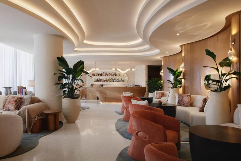 Elegant hotel lounge with curved ceilings, modern seating, plants, and marble bar area