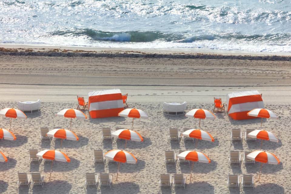 Organized beach setup with orange and white umbrellas, chairs, and cabanas facing the ocean