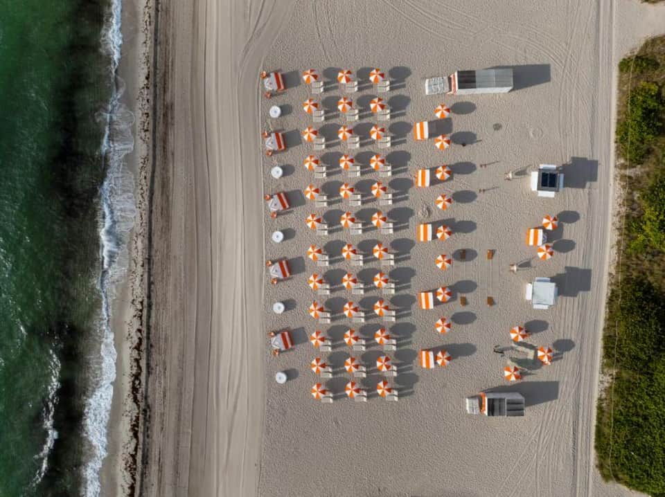 Aerial view of organized beach with colorful umbrellas, loungers, and manicured landscaping along ocean waves