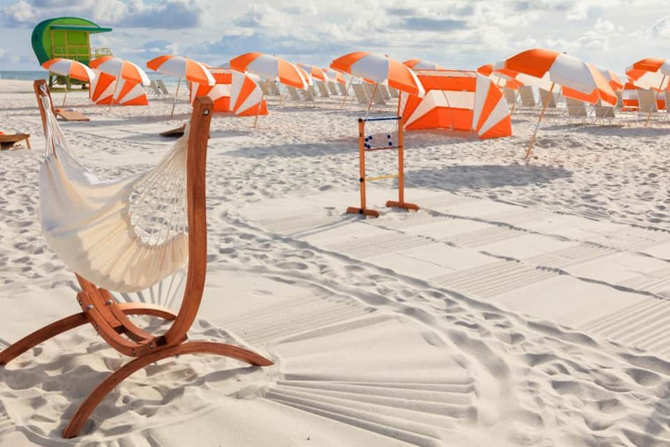Sandy beach with white hammock and orange-white beach umbrellas lined along shore