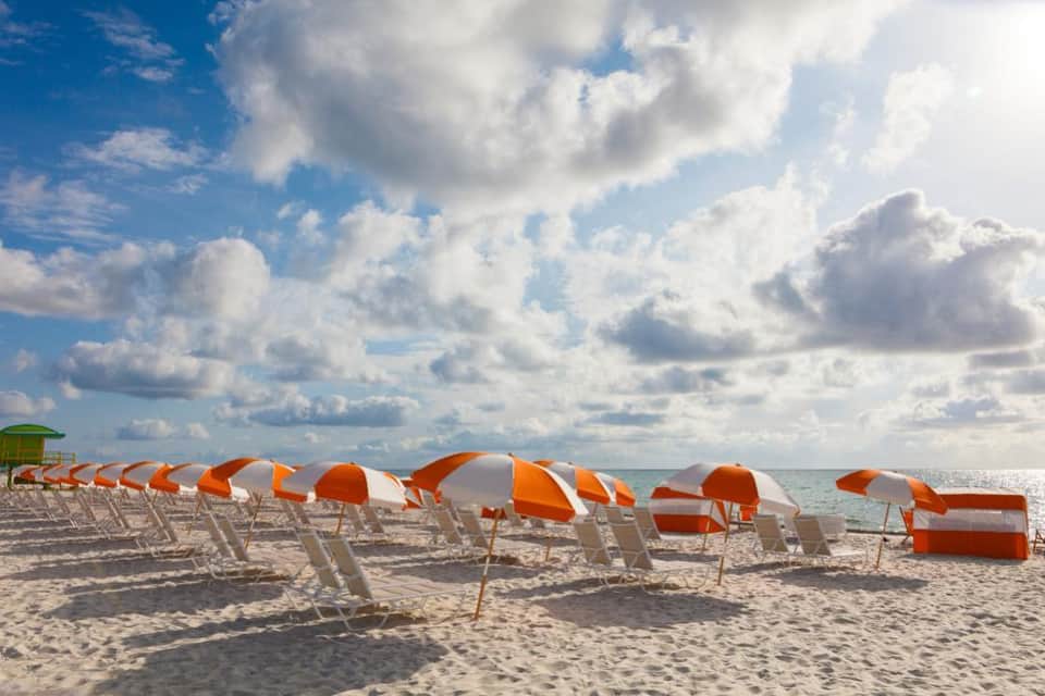 Rows of orange and white striped beach chairs arranged on sandy shore with ocean and cloudy sky