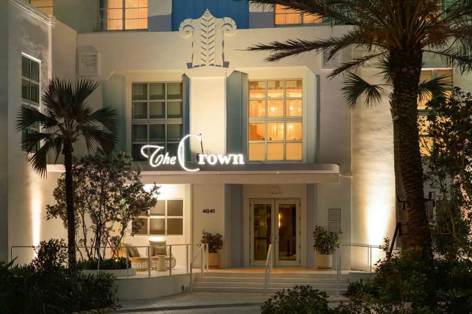 Art deco style hotel entrance facade with neon sign and illuminated palm trees at night