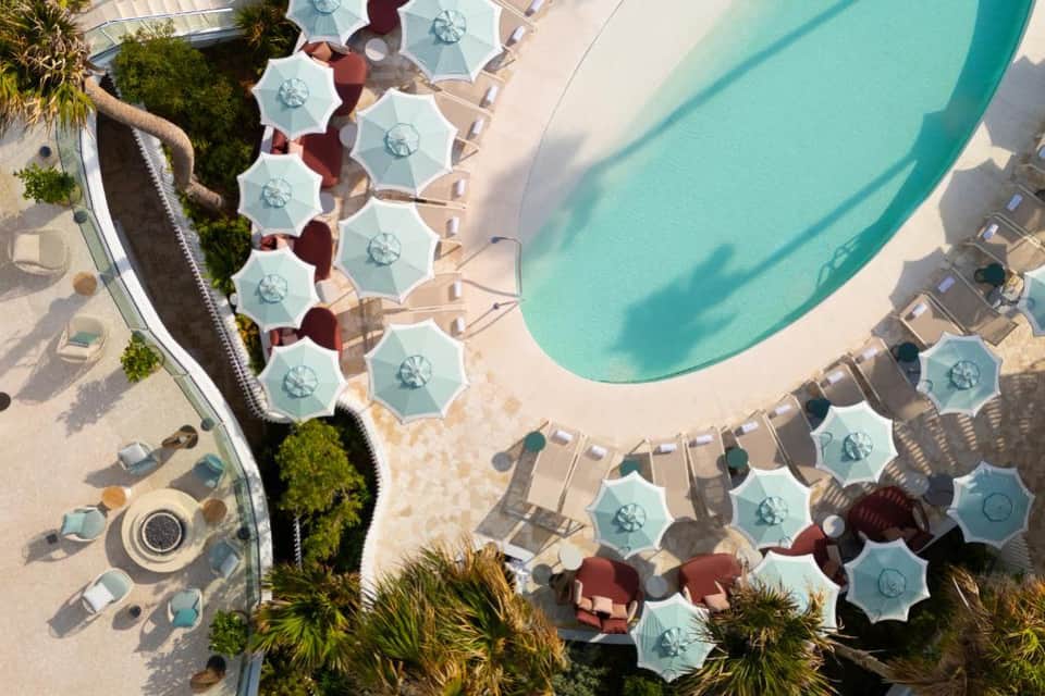 Aerial view of resort pool with turquoise water, lounge chairs, umbrellas, and palm landscaping