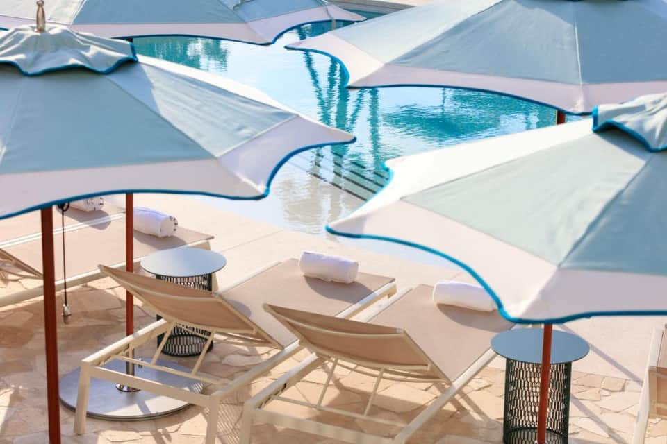Swimming pool with blue umbrellas, white loungers, and afternoon sunlight