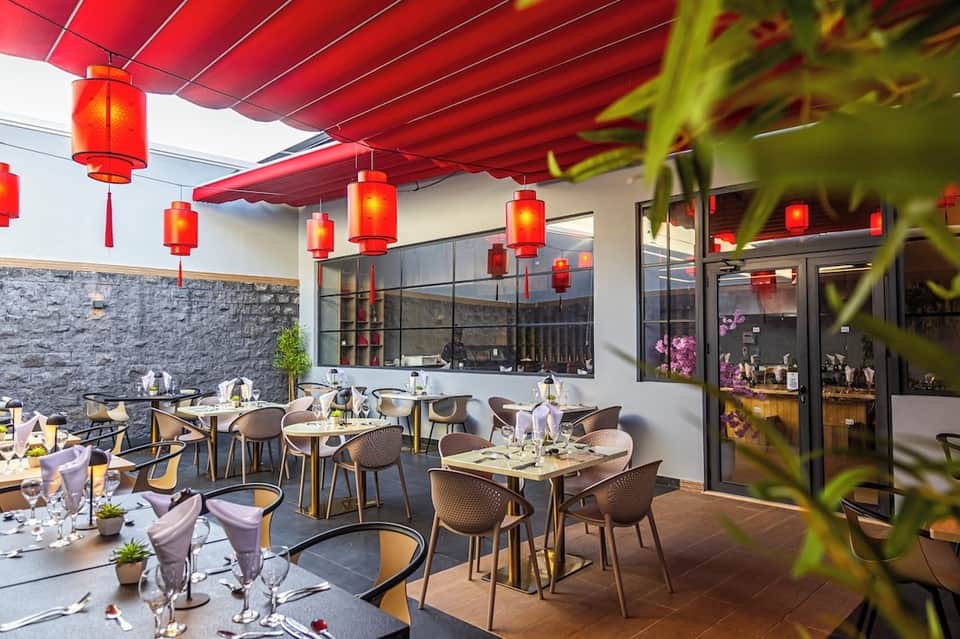 Outdoor dining terrace with red awning, red Chinese lanterns, modern chairs, tables, and stone wall accents