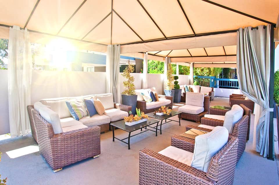 Covered outdoor lounge area with wicker furniture, cream cushions, and flowing white curtains in a luxury resort setting