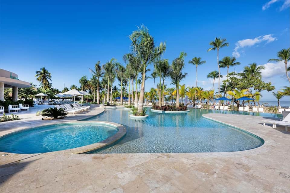 Resort lagoon pool with palm trees, white umbrellas, and waterfront view