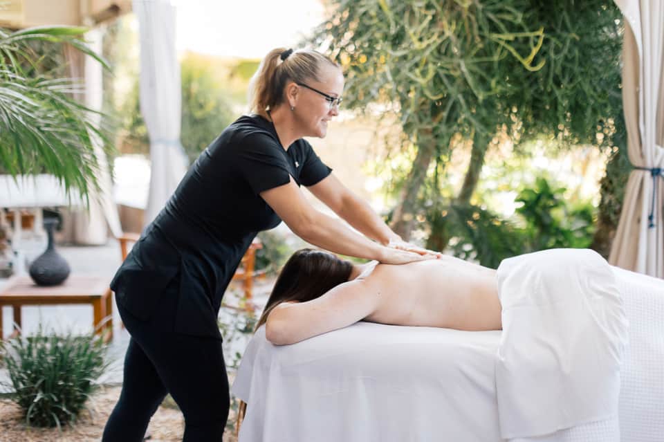 Outdoor spa massage treatment with therapist and client in garden setting with greenery
