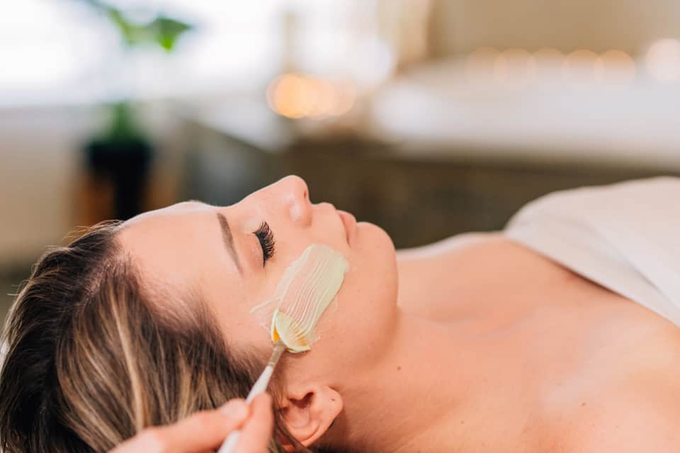 Woman receiving facial treatment with green skincare mask at spa