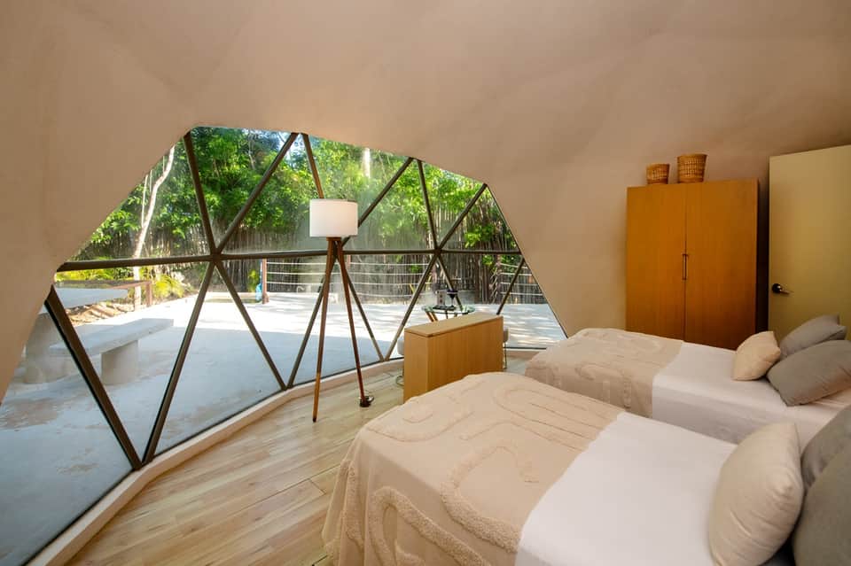 Bright guest room with two beds, geometric window frame, wooden wardrobe, and mountain forest view