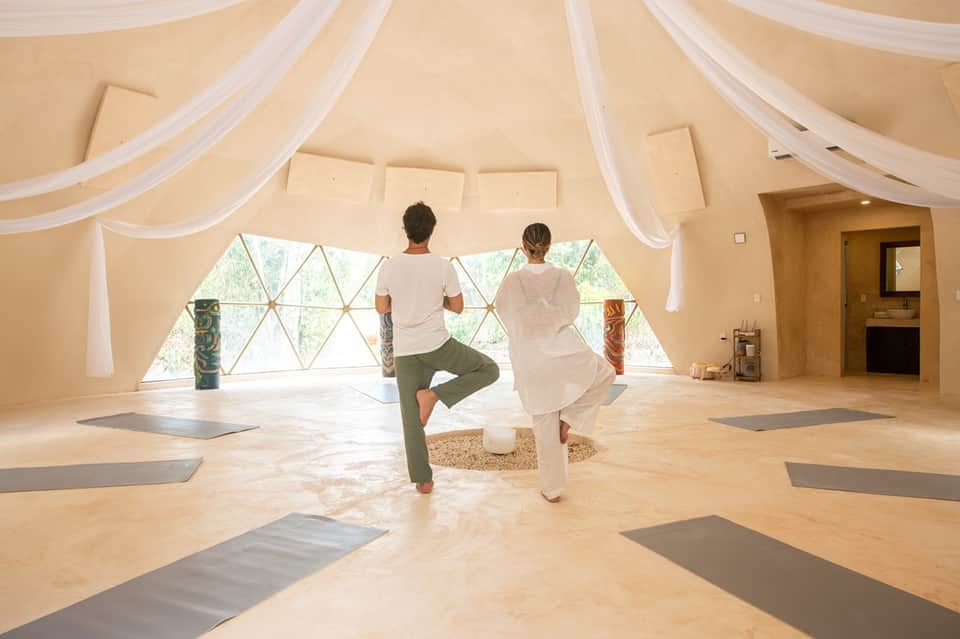 Couple practicing yoga in a bright dome-shaped studio with large geometric windows and wooden floors