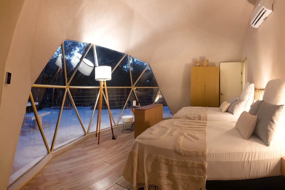 Modern geodesic dome bedroom with geometric windows, white bedding, wooden wardrobe, and nighttime views
