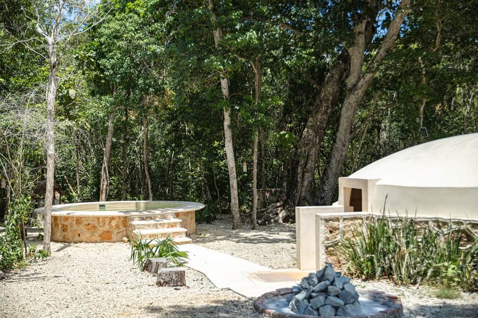 Outdoor hot tub in forest clearing with fire pit and glamping tent
