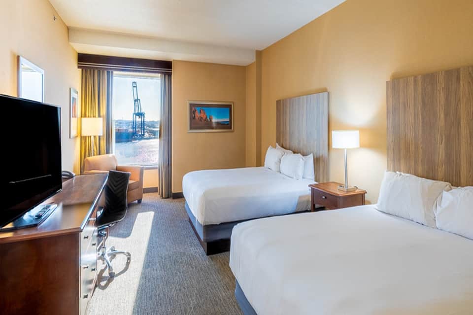 Hotel room with two queen beds, warm yellow walls, and port terminal view through window