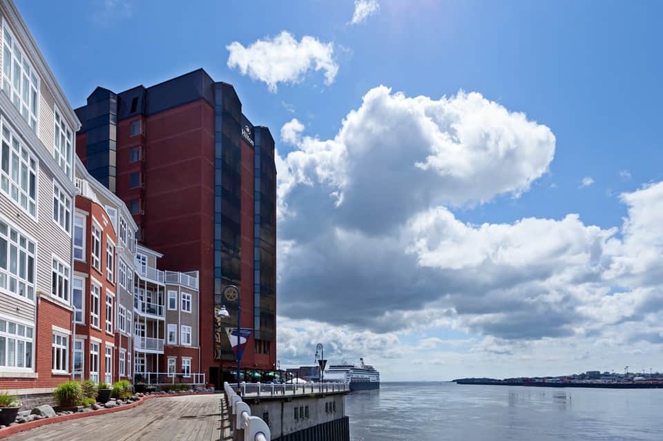 Waterfront hotel building with red brick facade overlooking river and cruise ship